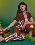 Alex is sitting on the ground wearing Paintstamped Pantry Button-Up in Mushroom and matching Work Pants