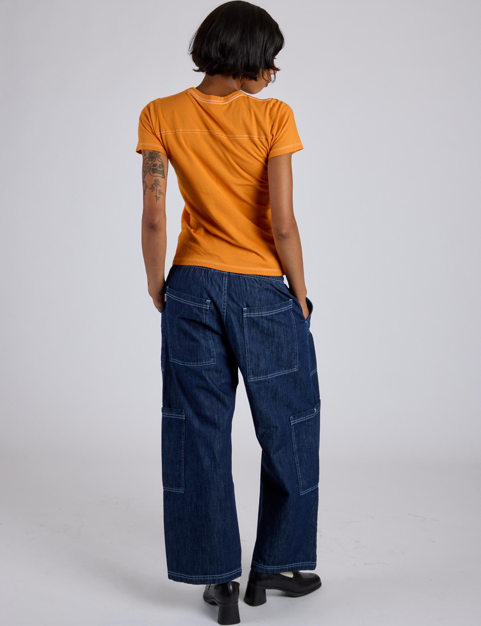 Back view of Jr. Varsity Tee in Creamsicle Orange and dark wash Denim Drop Pocket Cargo pants on Kira