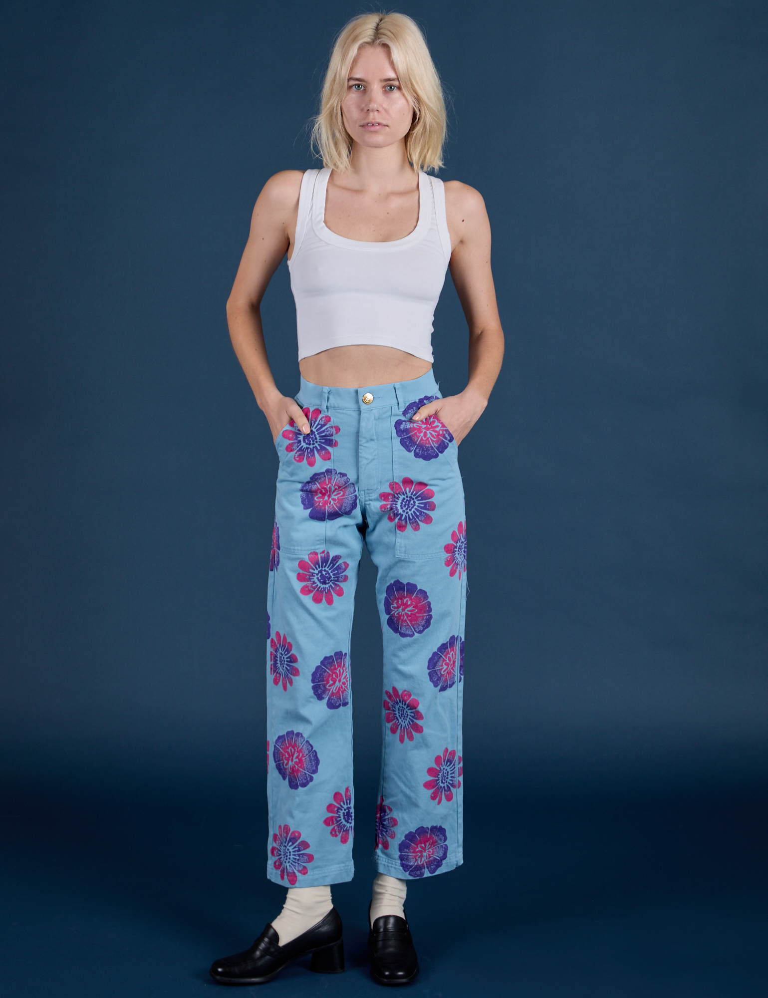 Madeline is 5’9” and wearing XXS Floral Painted Work Pants in Blue paired with a Cropped Tank in Vintage Tee White