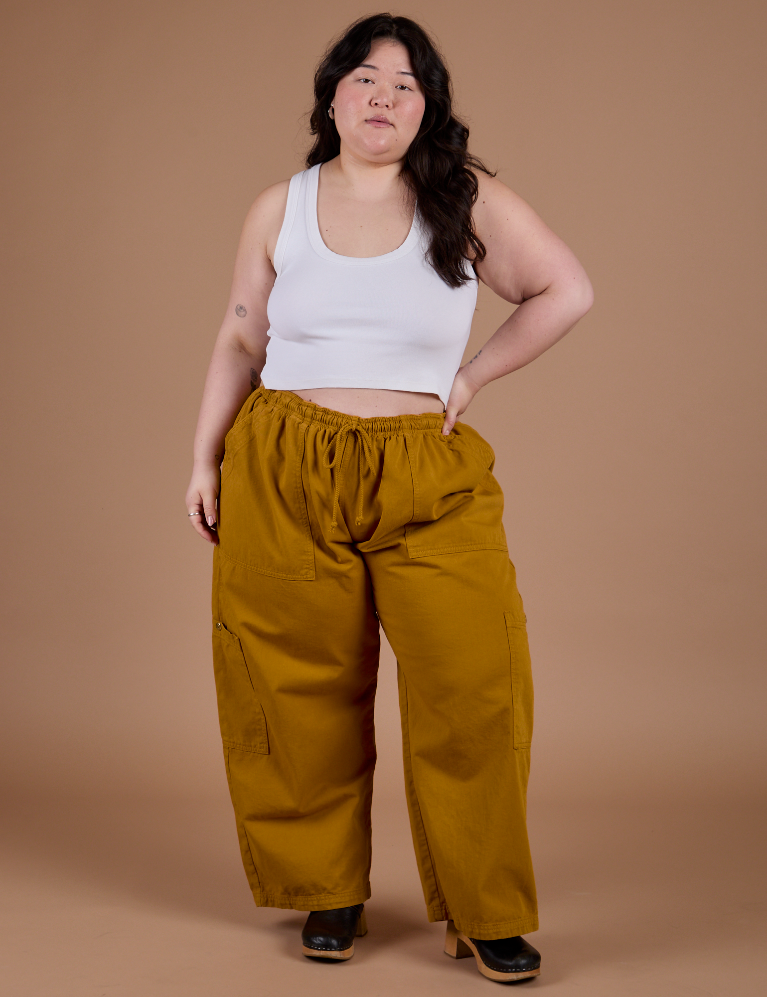 Ashley is 5'7" and wearing 1XL Drop Pocket Cargo Pants in Spicy Mustard paired with vintage tee white Cropped Tank