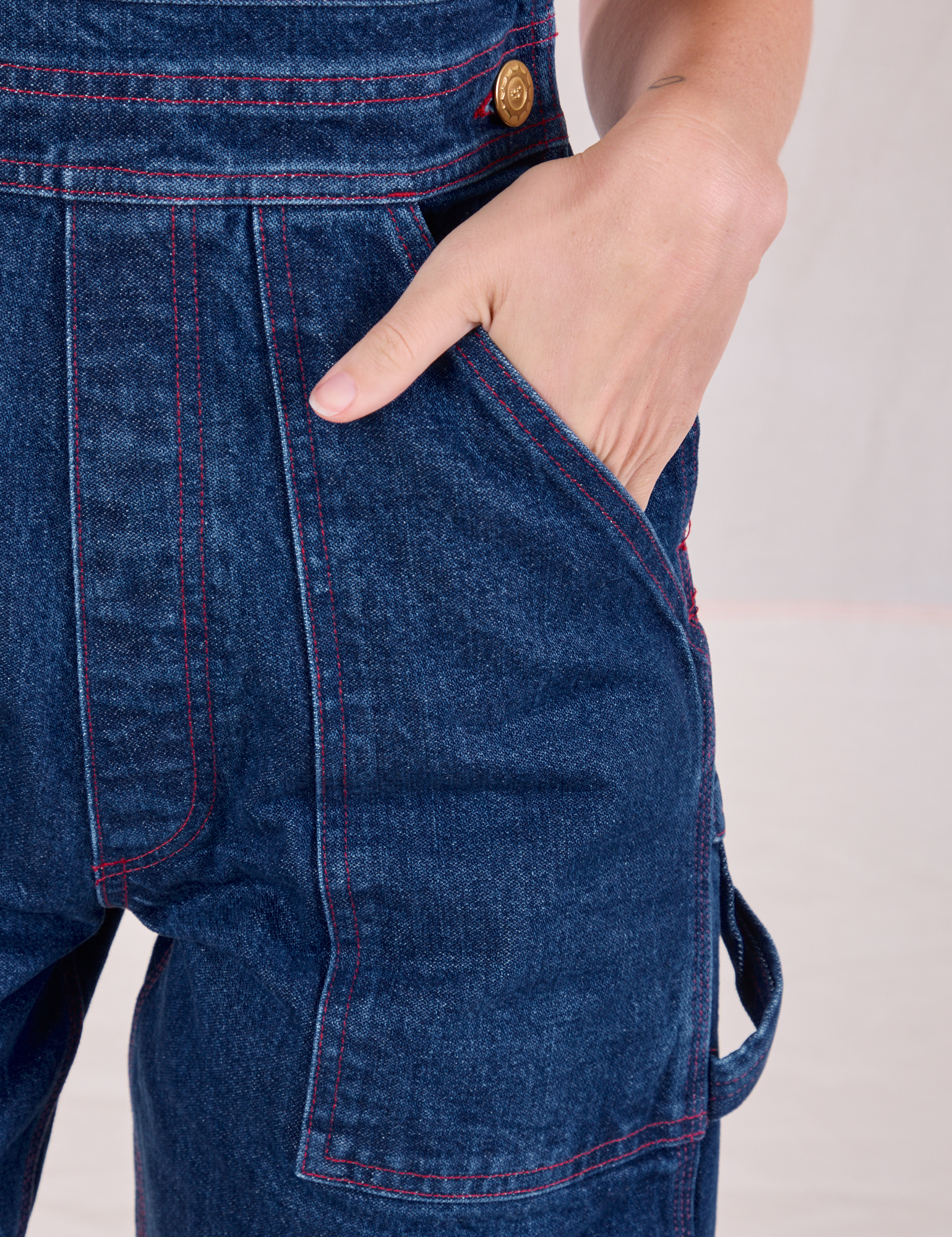 Close up of Alex's hand in the front pocket of Carpenter Overalls in Dark Wash