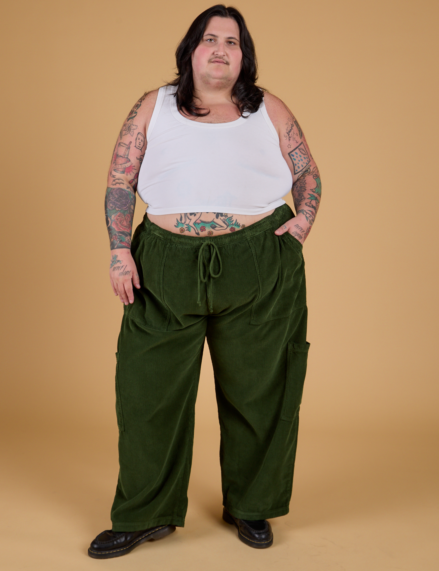 Sam is 5'10" and wearing 2XL Corduroy Drop Pocket Cargo Pants in Evergreen paired with a Cropped Tank in Vintage Tee White