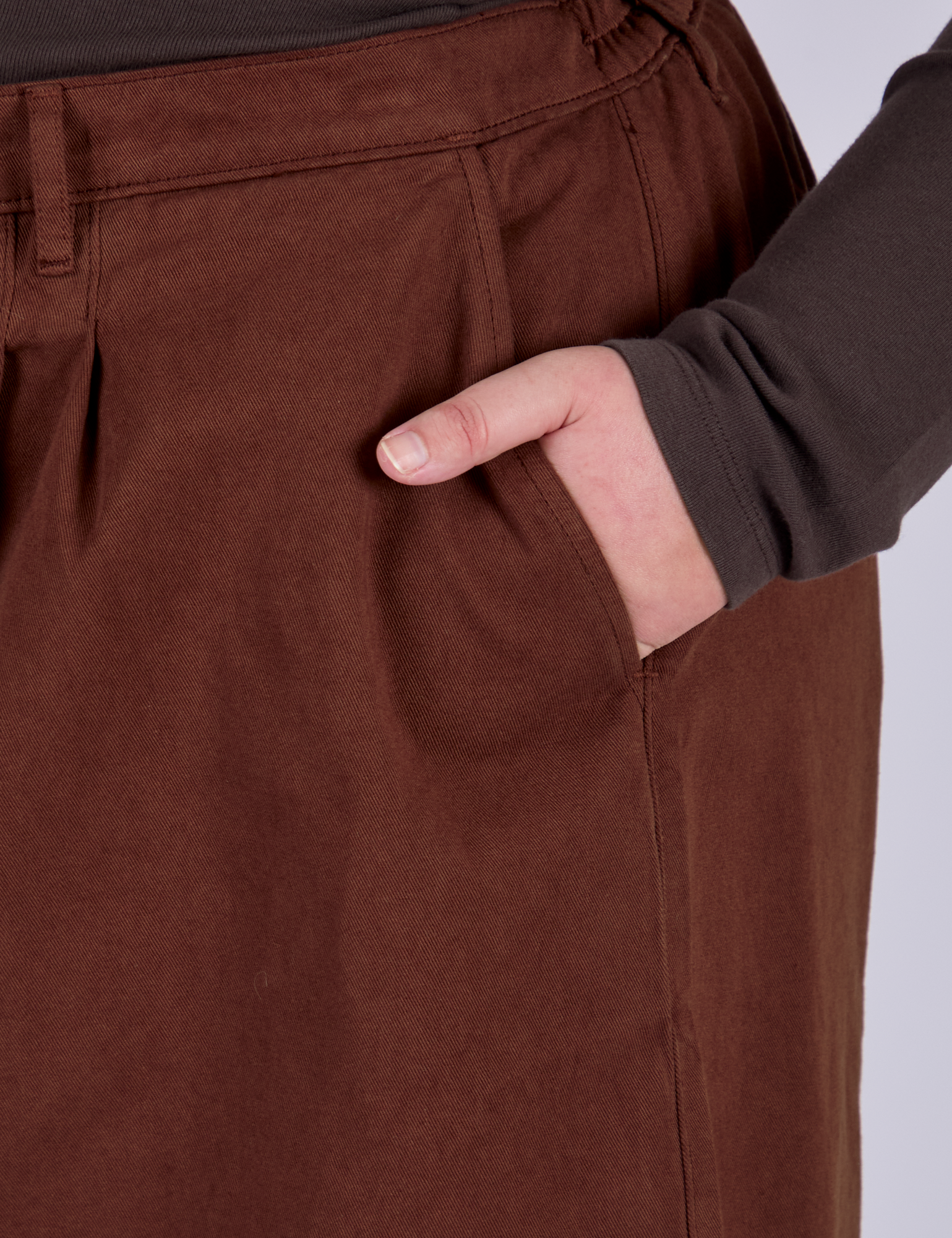 Close up of Juliet's hand in the front pocket of Pleated Trouser Shorts in Fudgesicle Brown