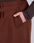 Close up of Juliet's hand in the front pocket of Pleated Trouser Shorts in Fudgesicle Brown