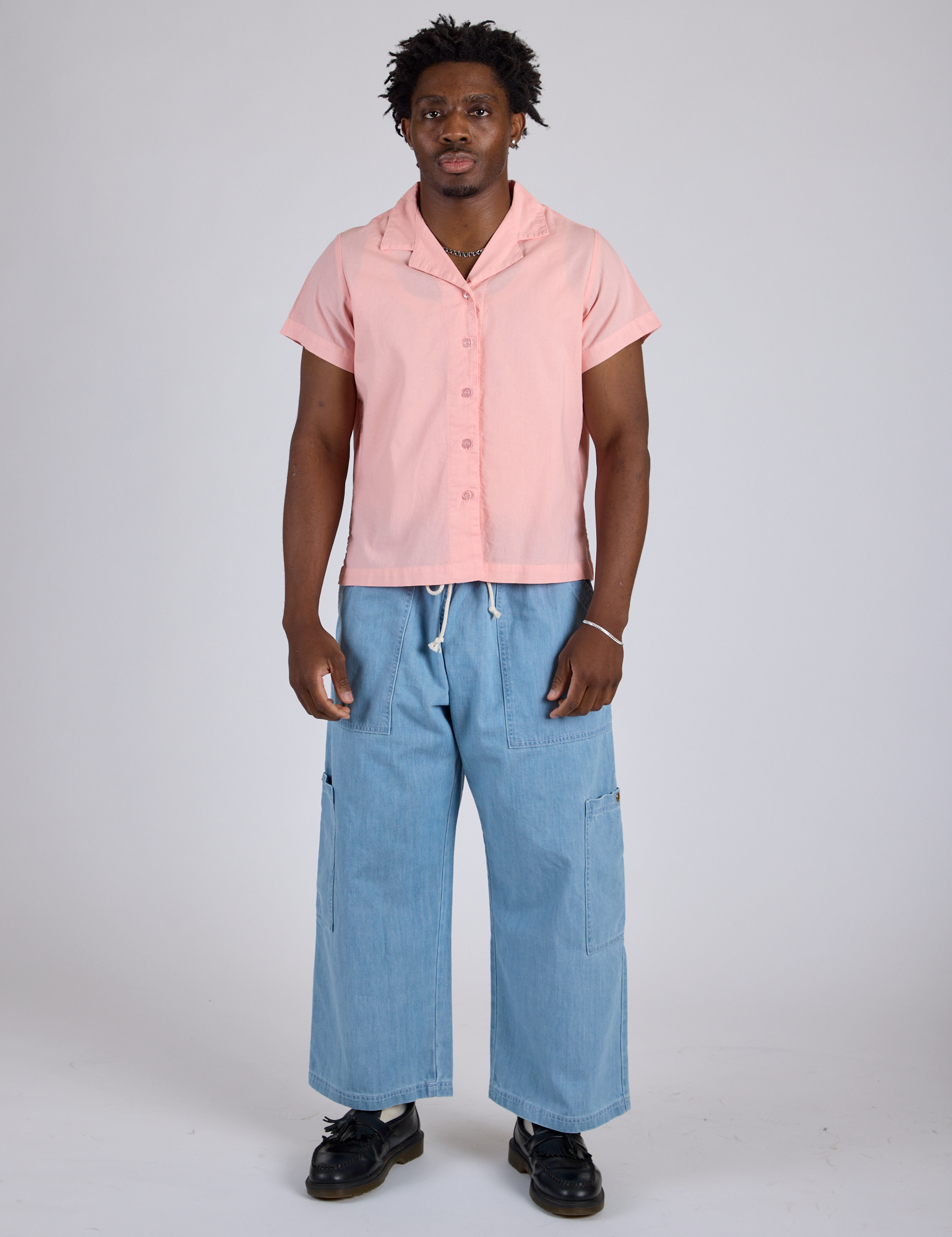 Isaac is wearing a buttoned up Pantry Button-Up in Baby Pink and light wash Denim Drop Pocket Pants