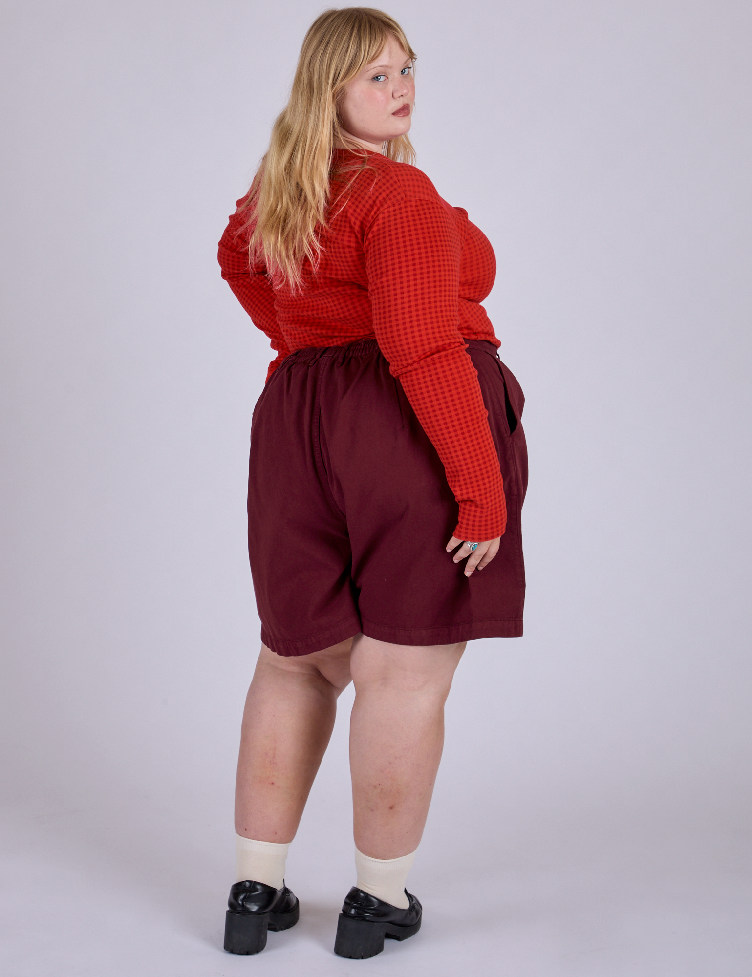 Angled back view of Pleated Trouser Shorts in Red Wine and mustang red Long Sleeve Gingham Baby Tee