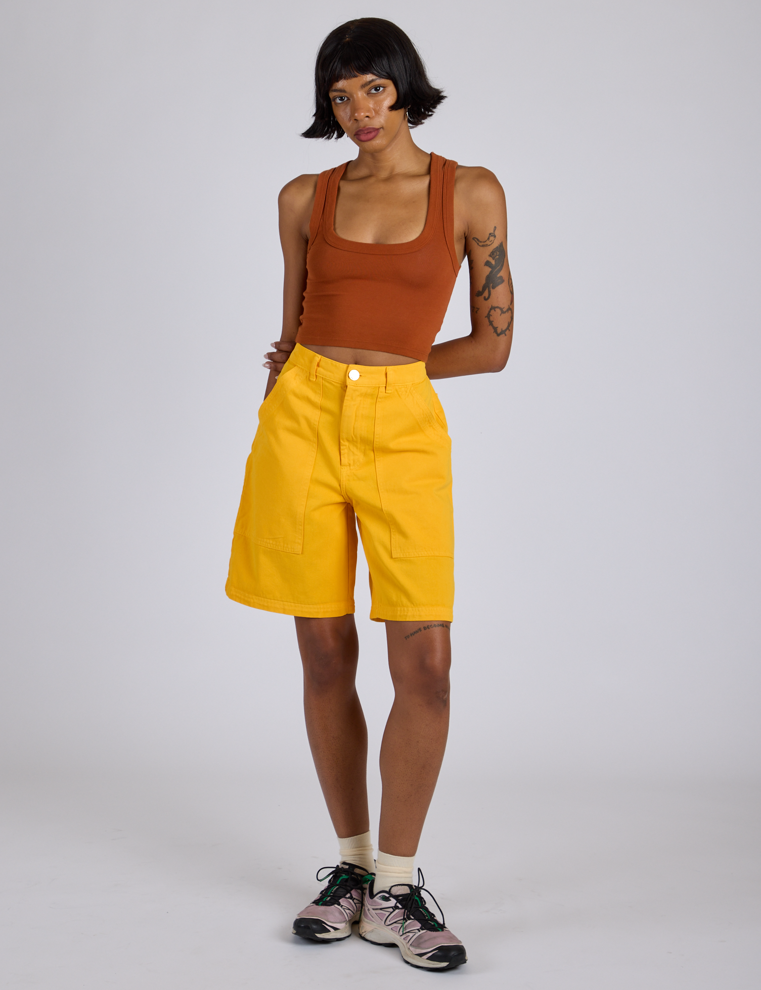 Kira is 5’10” and wearing XS Longline Work Shorts in Sunshine Yellow paired with burnt terracotta Cropped Tank