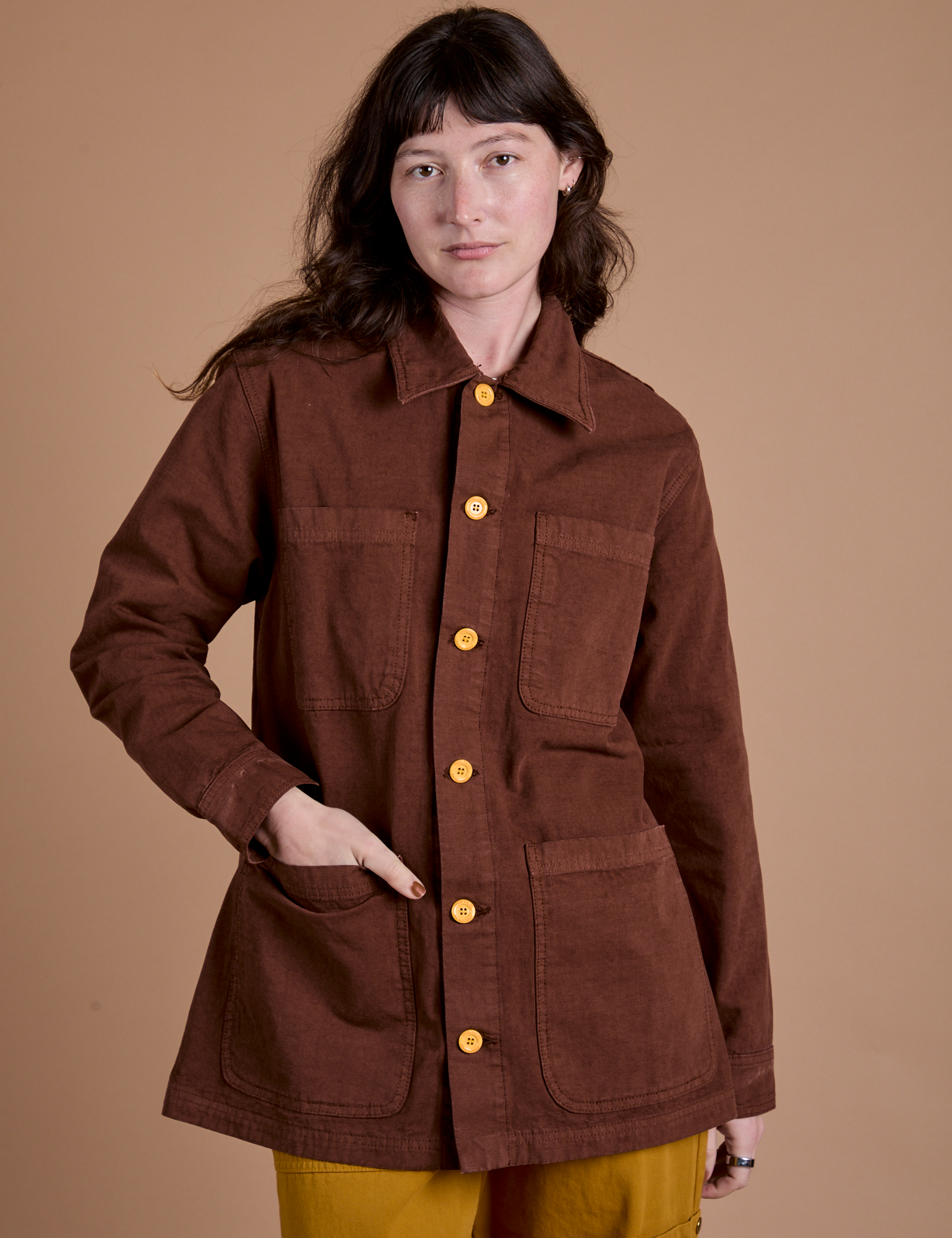 Alex is wearing a buttoned up Ripstop Field Coat in Fudgesicle Brown