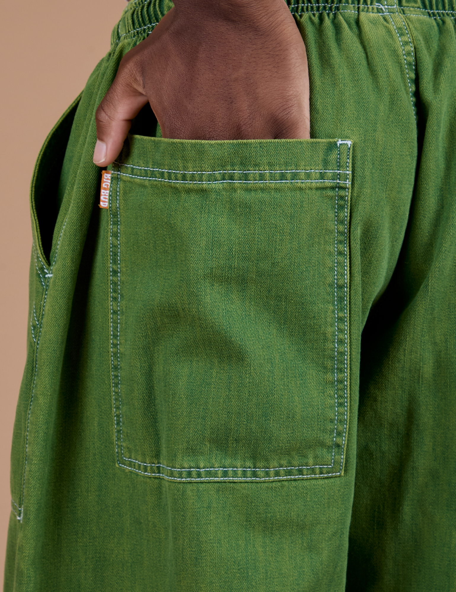 Close up of Isaac's hand in the back pocket of Denim Drop Pocket Pants in Green Overdye
