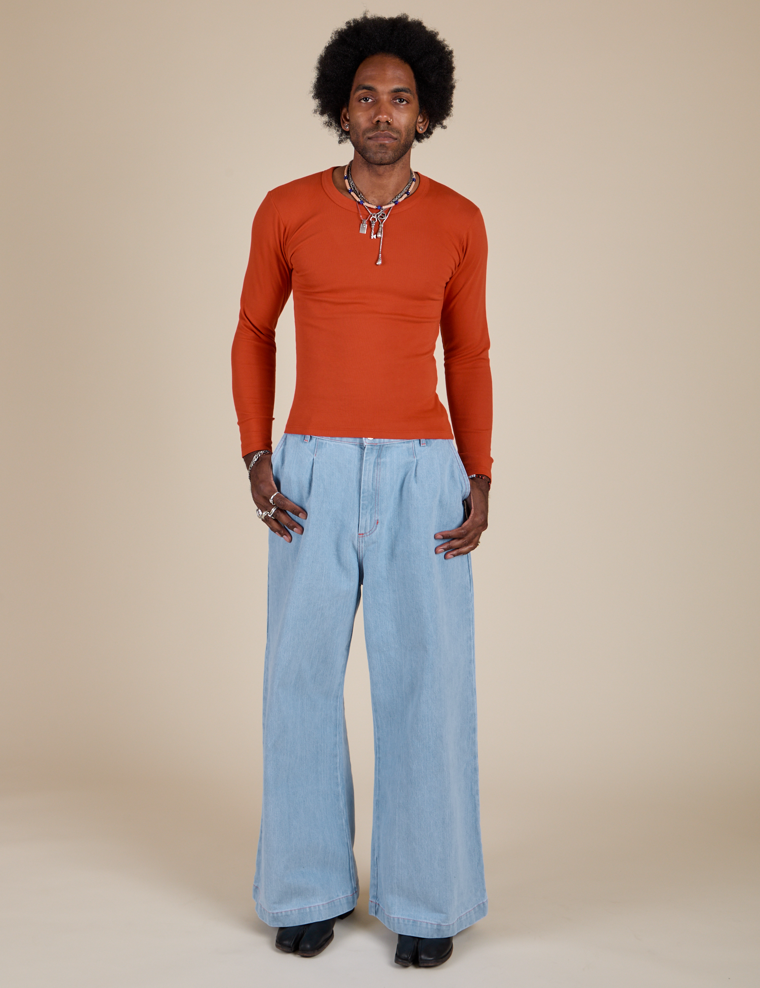 Jerrod is wearing Long Sleeve Baby Tee in Chili Red and light wash Indigo Wide Leg Trousers