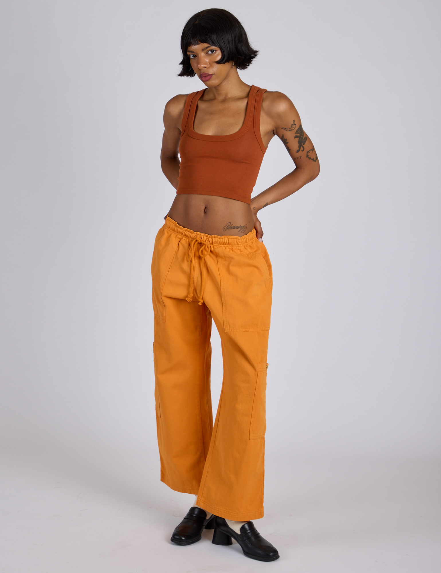 Kira is 5’10” and wearing XS Drop Pocket Cargo Pants in Creamsicle Orange paired with burnt terracotta Cropped Tank