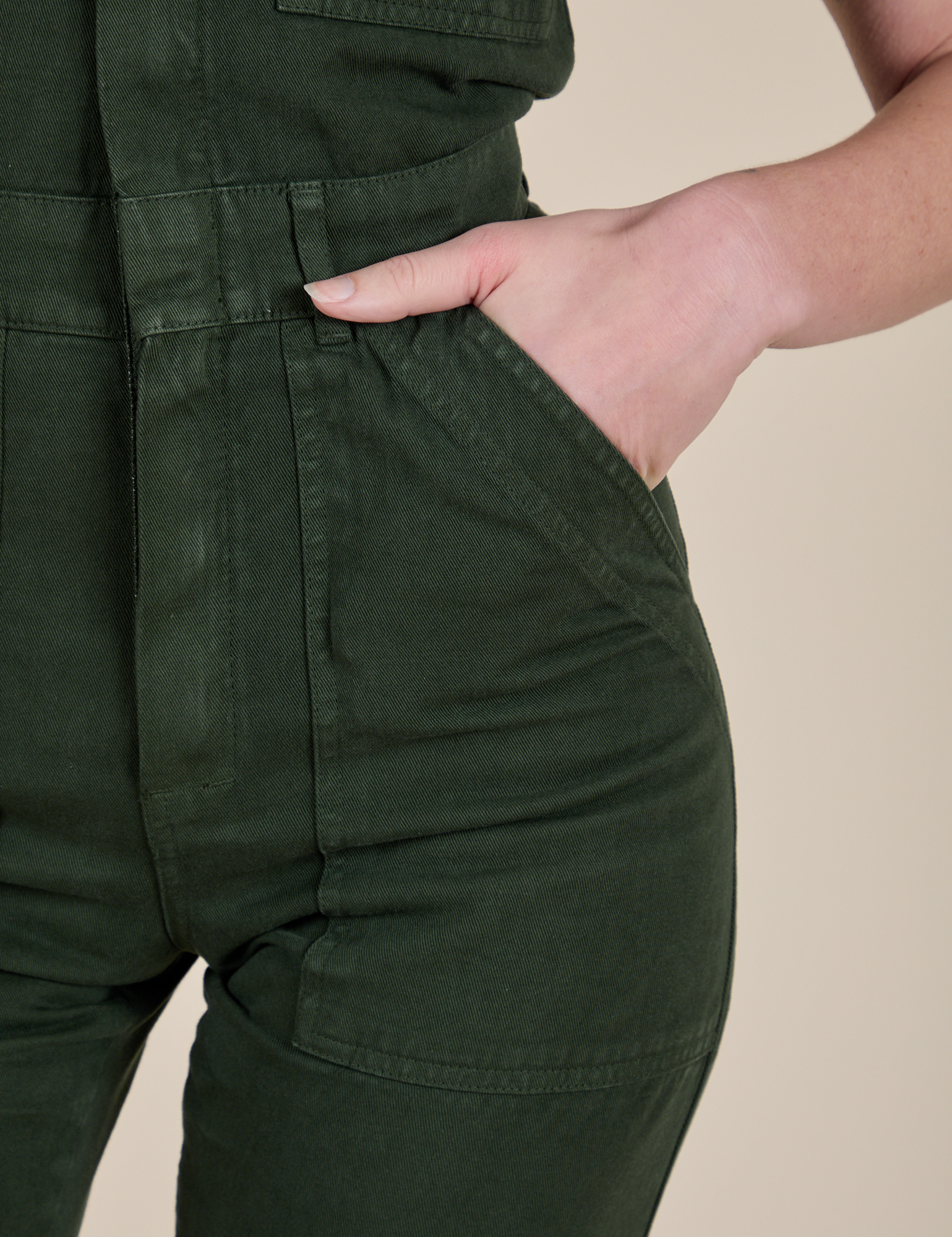 Close up of Alex's hand in the front pocket of Short Sleeve Jumpsuit in Swamp Green