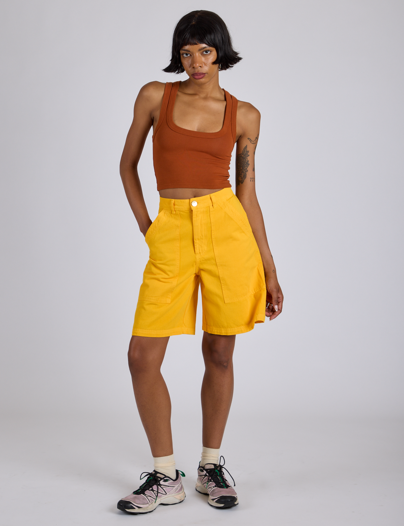 Kira is wearing Longline Work Shorts in Sunshine Yellow and burnt terracotta Cropped Tank