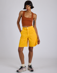 Kira is wearing Longline Work Shorts in Sunshine Yellow and burnt terracotta Cropped Tank