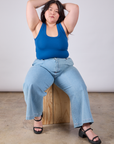 Ashley is sitting on a wooden block and wearing Cropped Tank Top in Royal Blue paired with light wash Indigo Wide Leg Trousers