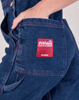 Close up of Alex's hand in the back pocket of Carpenter Overalls in Dark Wash