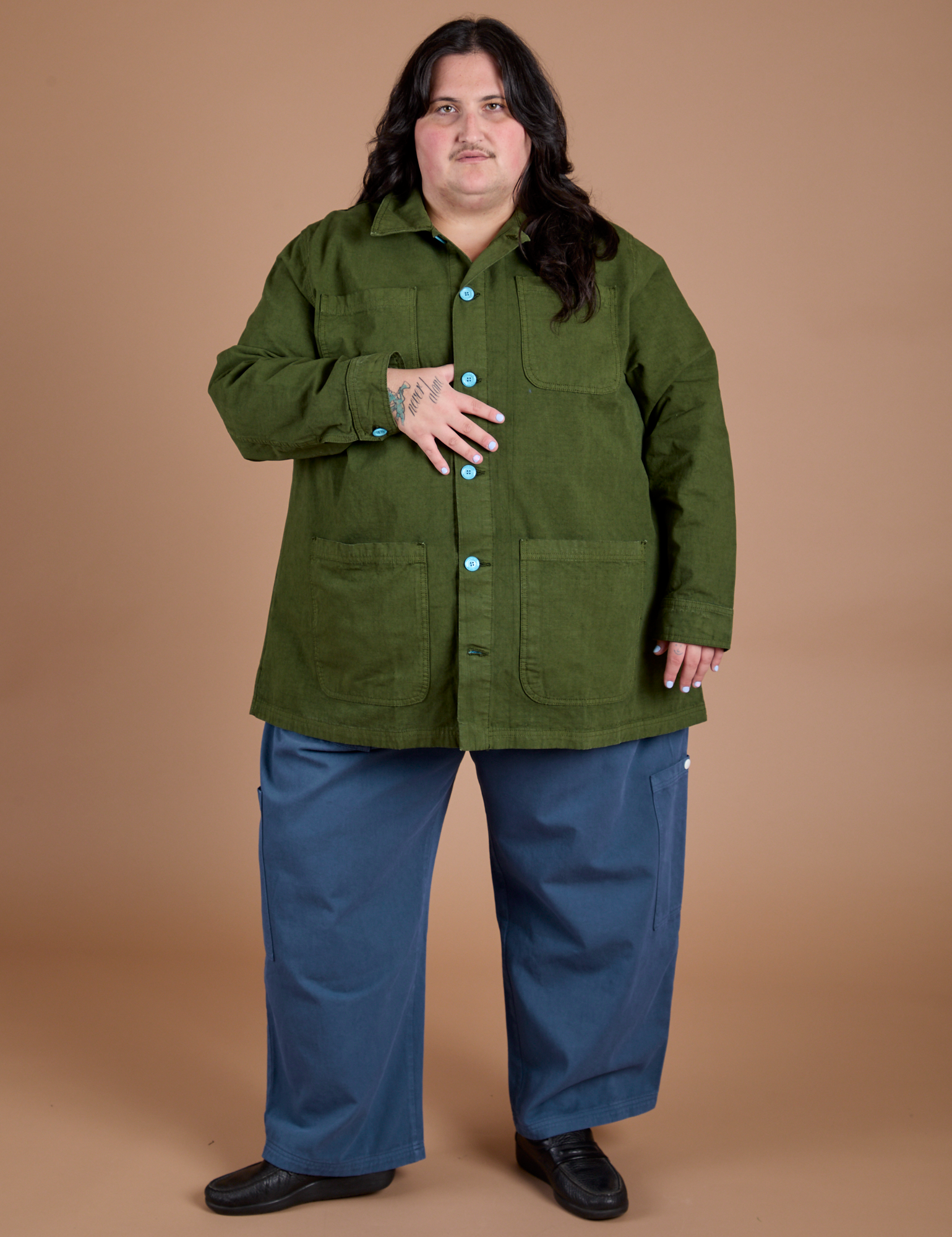 Sam is wearing a buttoned up Ripstop Field Coat in Evergreen with french blue Drop Pocket Cargo Pants