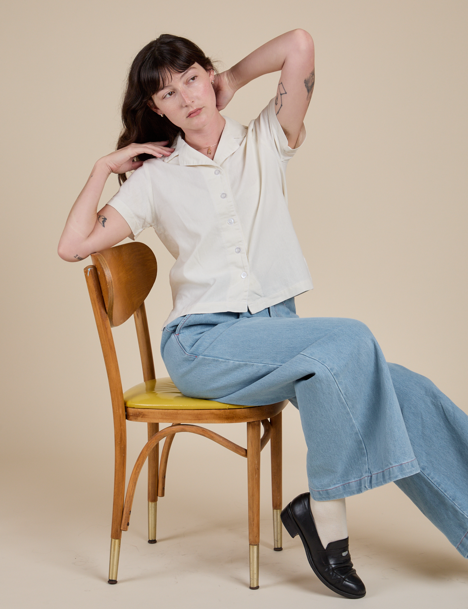 Pantry Button-Up in Vintage Tee White and light wash Indigo Wide Leg Trousers on Alex sitting on a chair