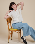 Pantry Button-Up in Vintage Tee White and light wash Indigo Wide Leg Trousers on Alex sitting on a chair