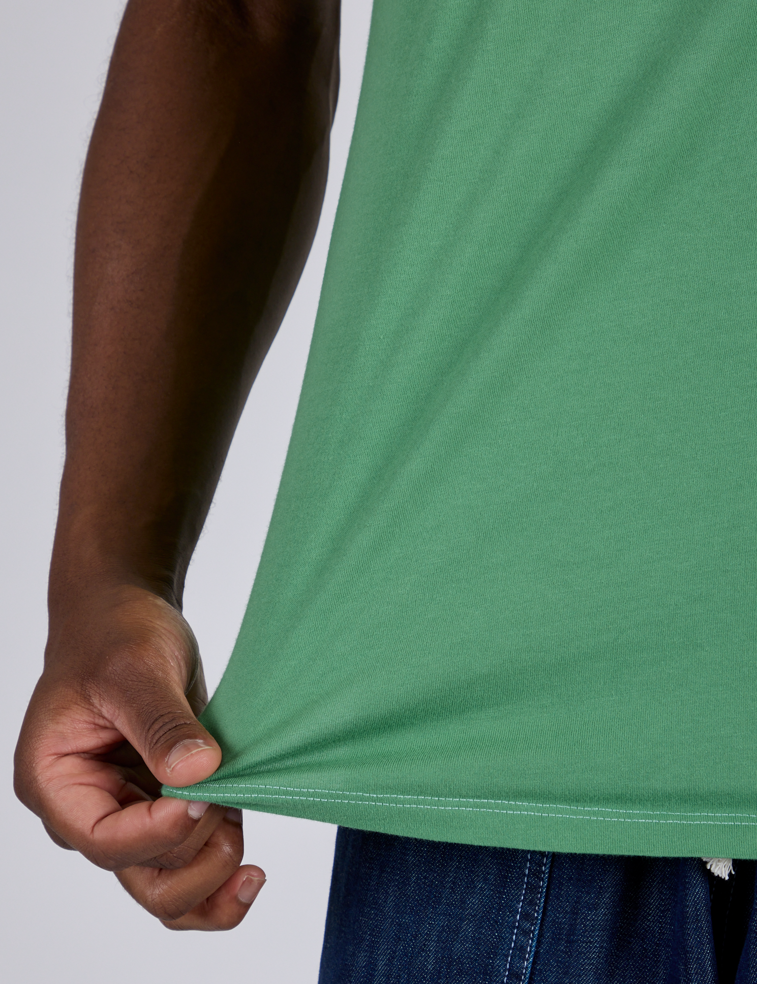Close up of Isaac pulling the bottom hem of Jr. Varsity Tee in Seafoam Green