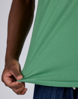 Close up of Isaac pulling the bottom hem of Jr. Varsity Tee in Seafoam Green