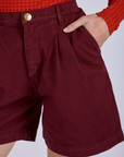 Close up of Alex's hand in the front pocket of Pleated Trouser Shorts in Red Wine