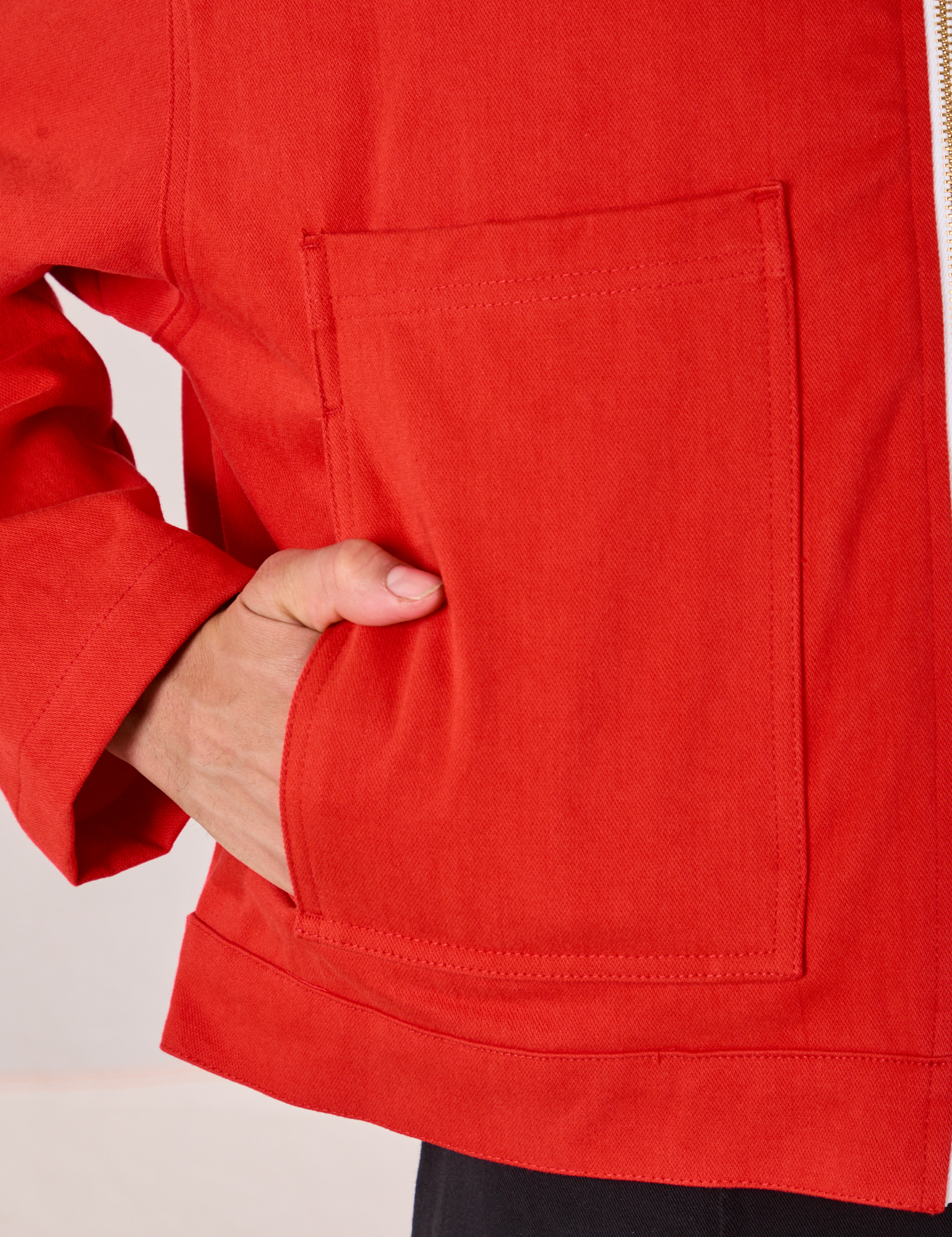 Close up of Anthony's hand in the front pocket of Mechanic Jacket in Mustang Red