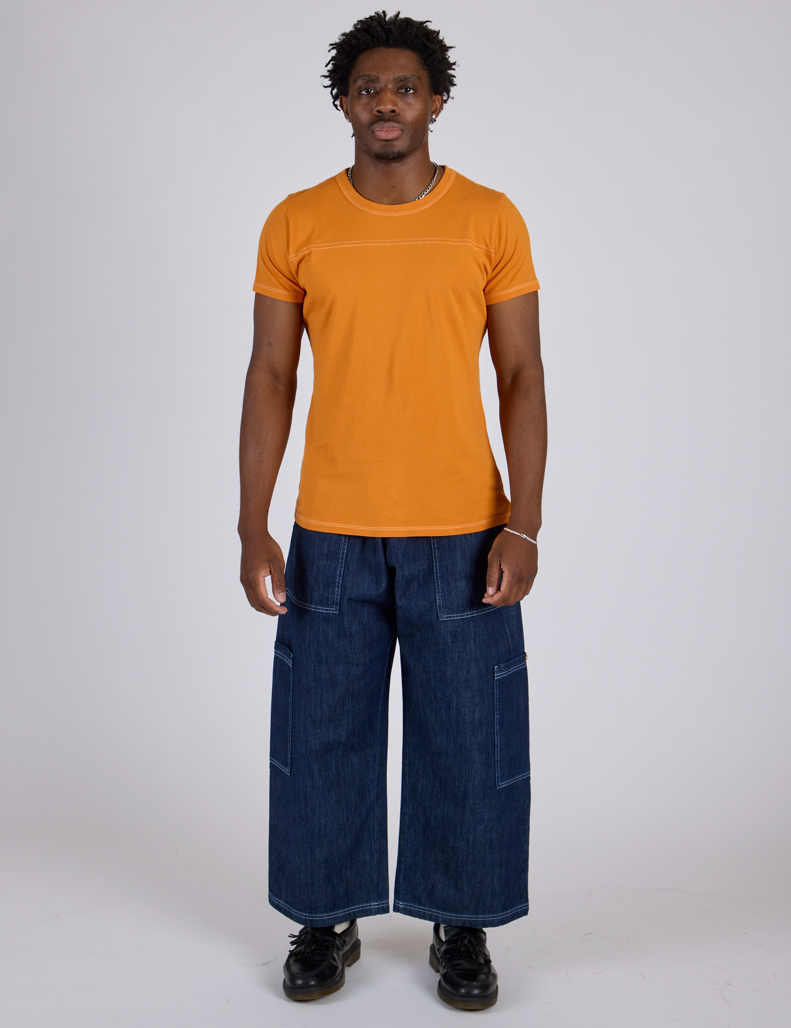 Isaac is 5’10” and wearing M Jr. Varsity Tee in Creamsicle Orange paired with dark wash Denim Drop Pocket Pants