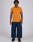 Isaac is 5’10” and wearing M Jr. Varsity Tee in Creamsicle Orange paired with dark wash Denim Drop Pocket Pants