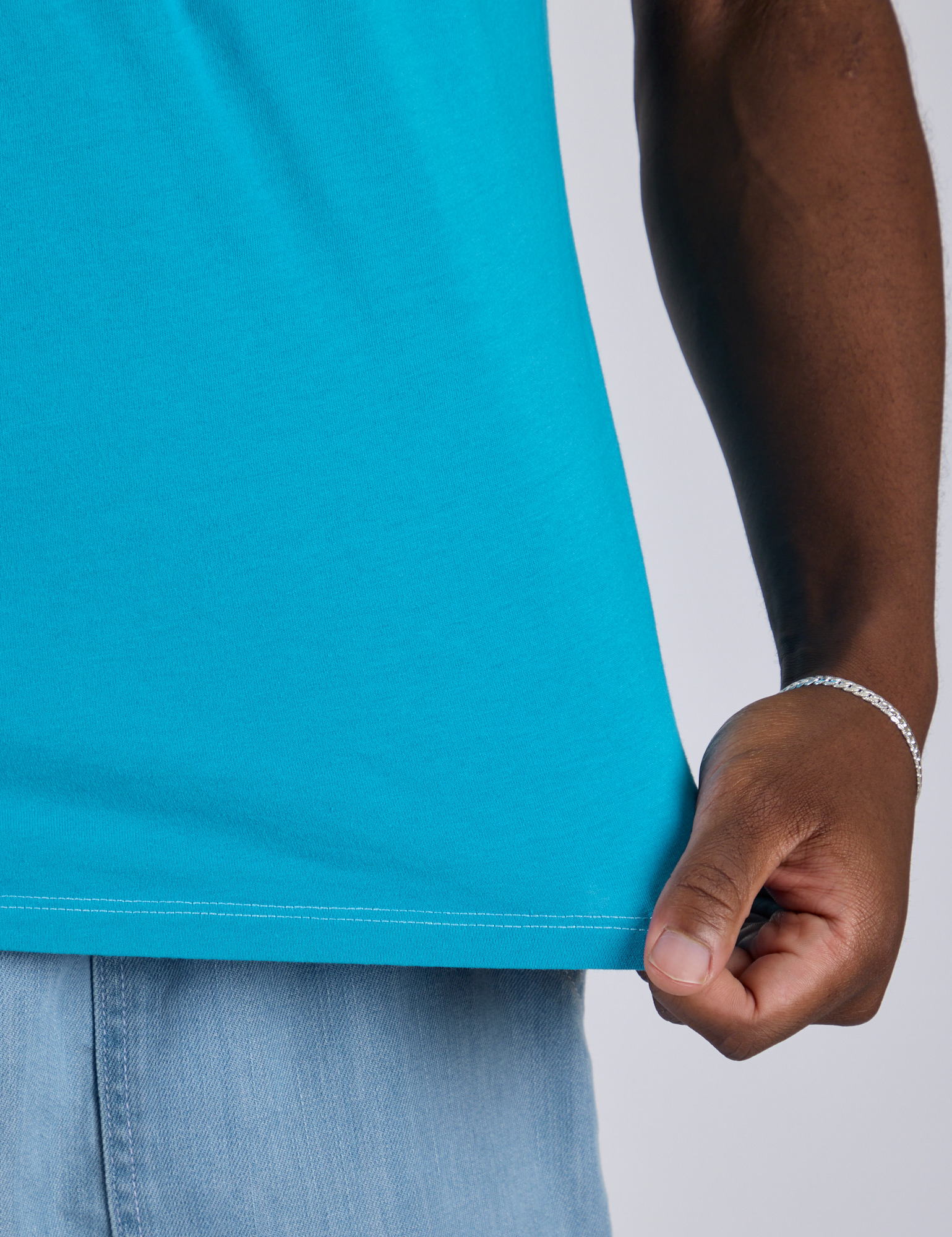 Close up of Isaac tugging the bottom hem of Jr. Varsity Tee in Hawaiian Blue