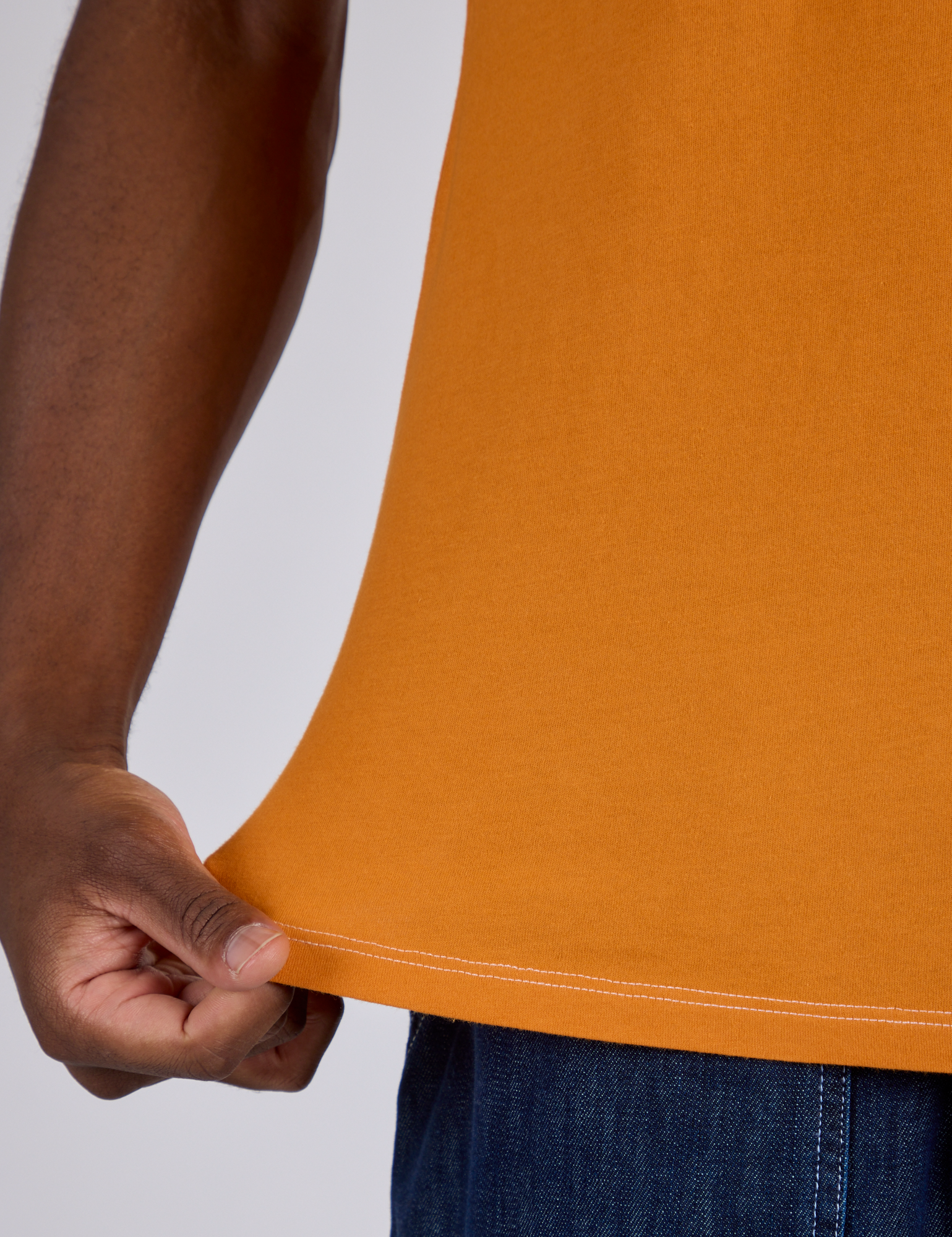 Close up of Isaac pulling on the bottom hem of Jr. Varsity Tee in Creamsicle Orange