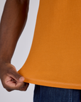 Close up of Isaac pulling on the bottom hem of Jr. Varsity Tee in Creamsicle Orange