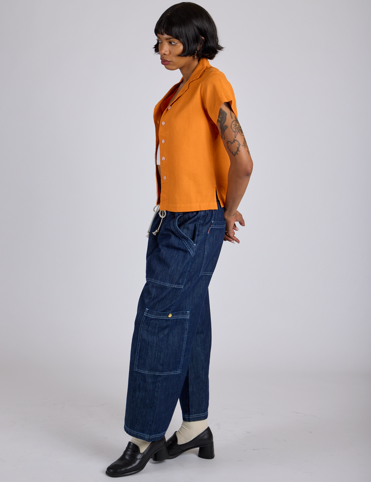 Side view of Pantry Button-Up in Creamsicle Orange and dark wash Denim Drop Pocket Pants on Kira