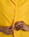 Close up of Kira buttoning the Pantry Button-Up in Sunshine Yellow