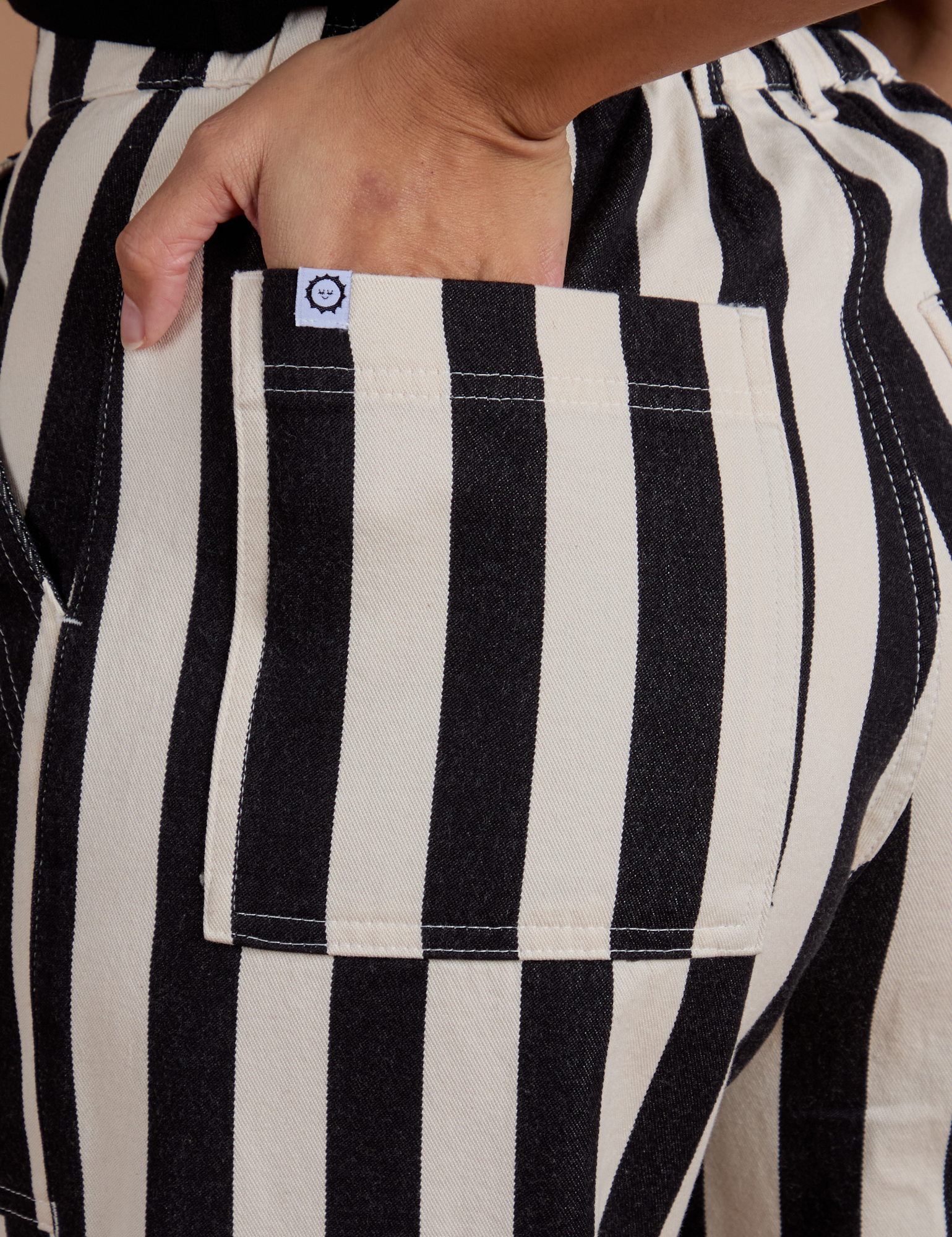 Close up of Tiara's hand in the back pocket of Black Stripe Work Pants in White