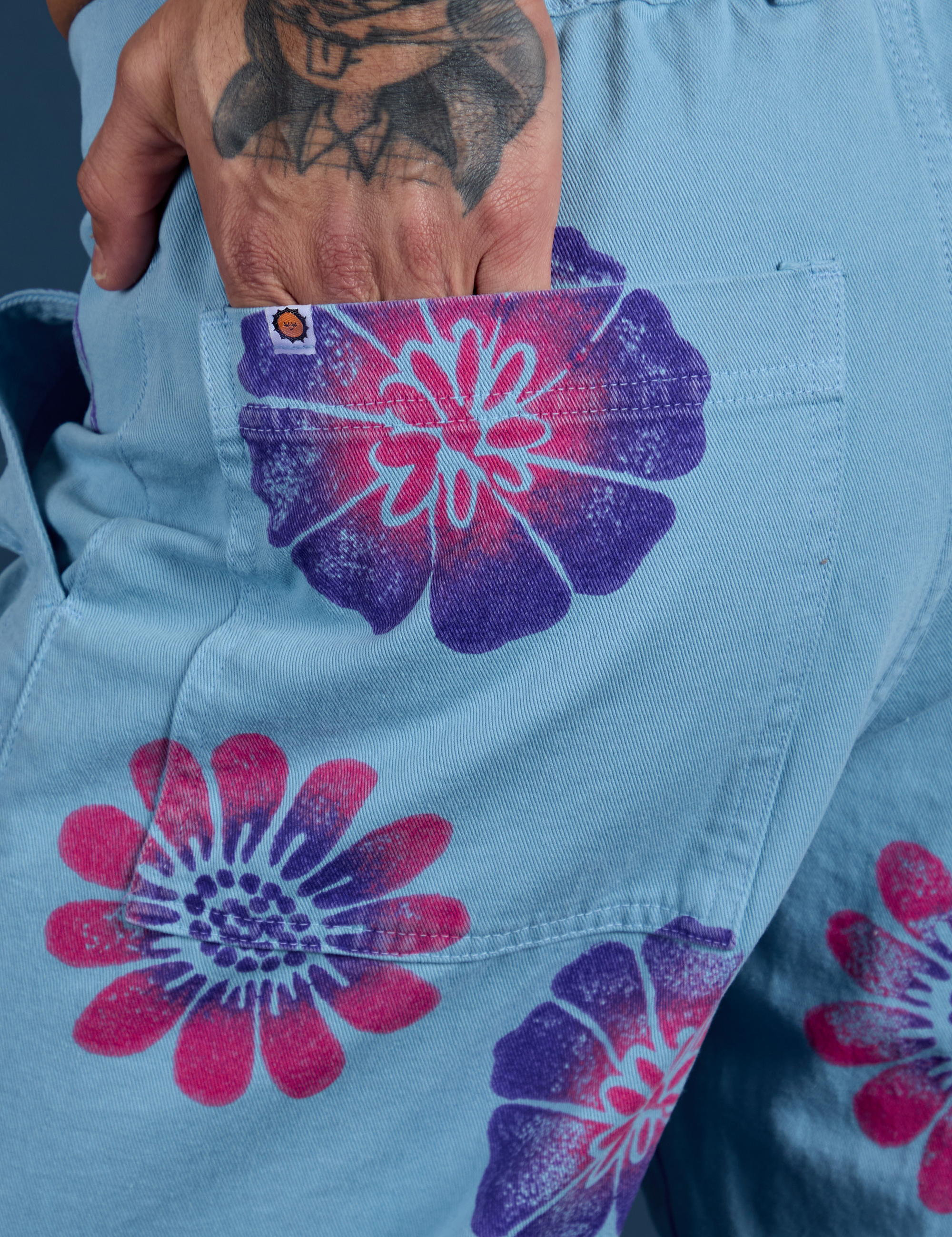 Close up of Jesse's hand in the back pocket of Floral Painted Work Pants in Blue