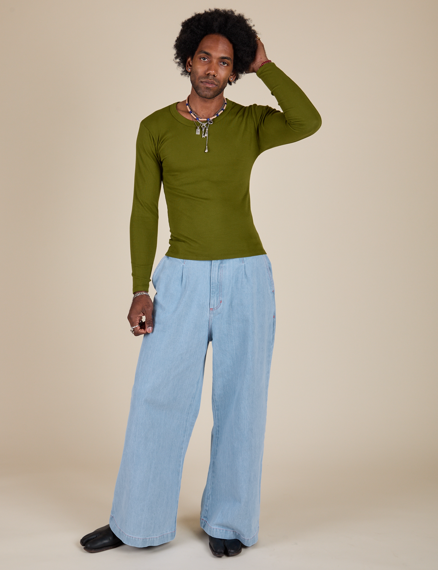 Jerrod is wearing Long Sleeve Baby Tee in Summer Olive and light wash Indigo Wide Leg Trousers