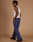 Side view of Railroad Denim Work Pants in Faded Grape Overdye and vintage tee off-white Tank Top on Isaac