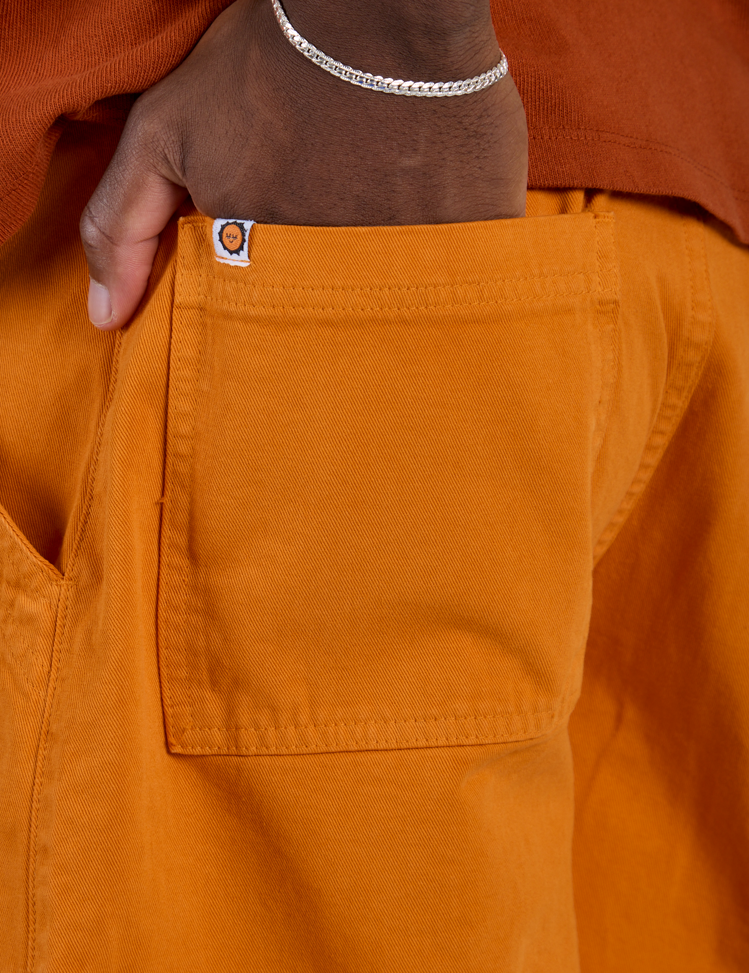 Close up of Isaac's hand in the back pocket of Longline Work Shorts in Creamsicle Orange