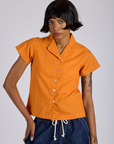 Kira is wearing a buttoned up Pantry Button-Up in Creamsicle Orange