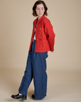Side view of Denim Work Jacket in Mustang Red and dark wash Indigo Wide Leg Trouser on Hana