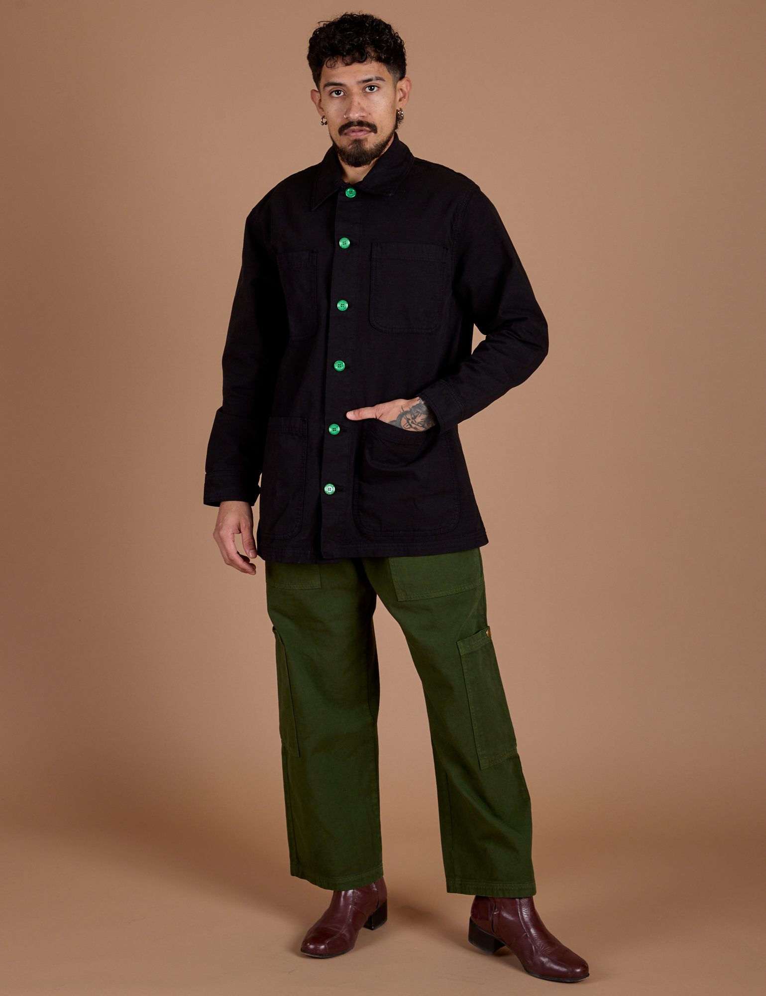 Jesse is wearing a buttoned up Ripstop Field Coat in Basic Black paired with evergreen Drop Pocket Cargo Pants