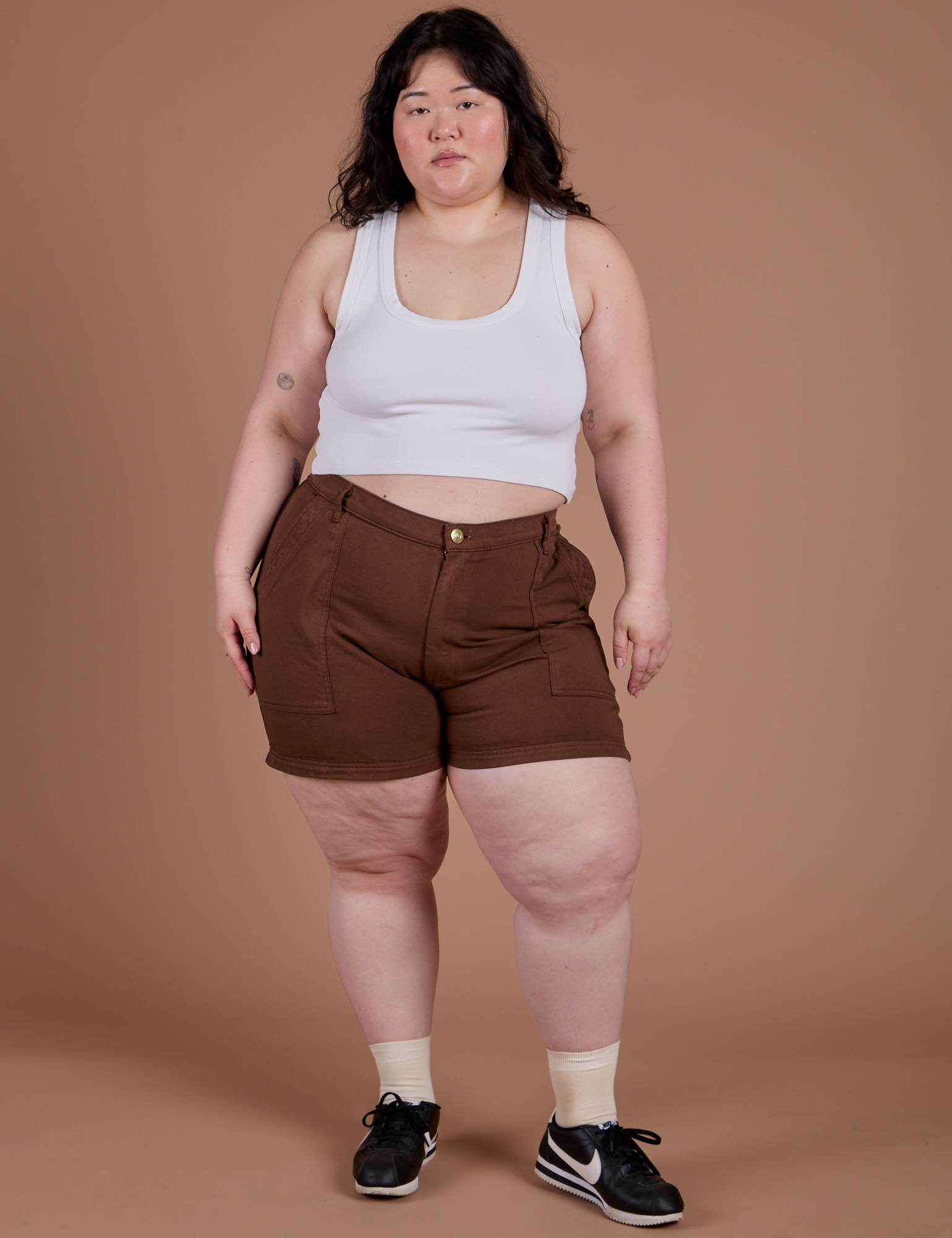 Ashley is 5’7” and wearing 1XL Classic Work Shorts in Fudgesicle Brown paired with a Cropped Tank in Vintage Tee White
