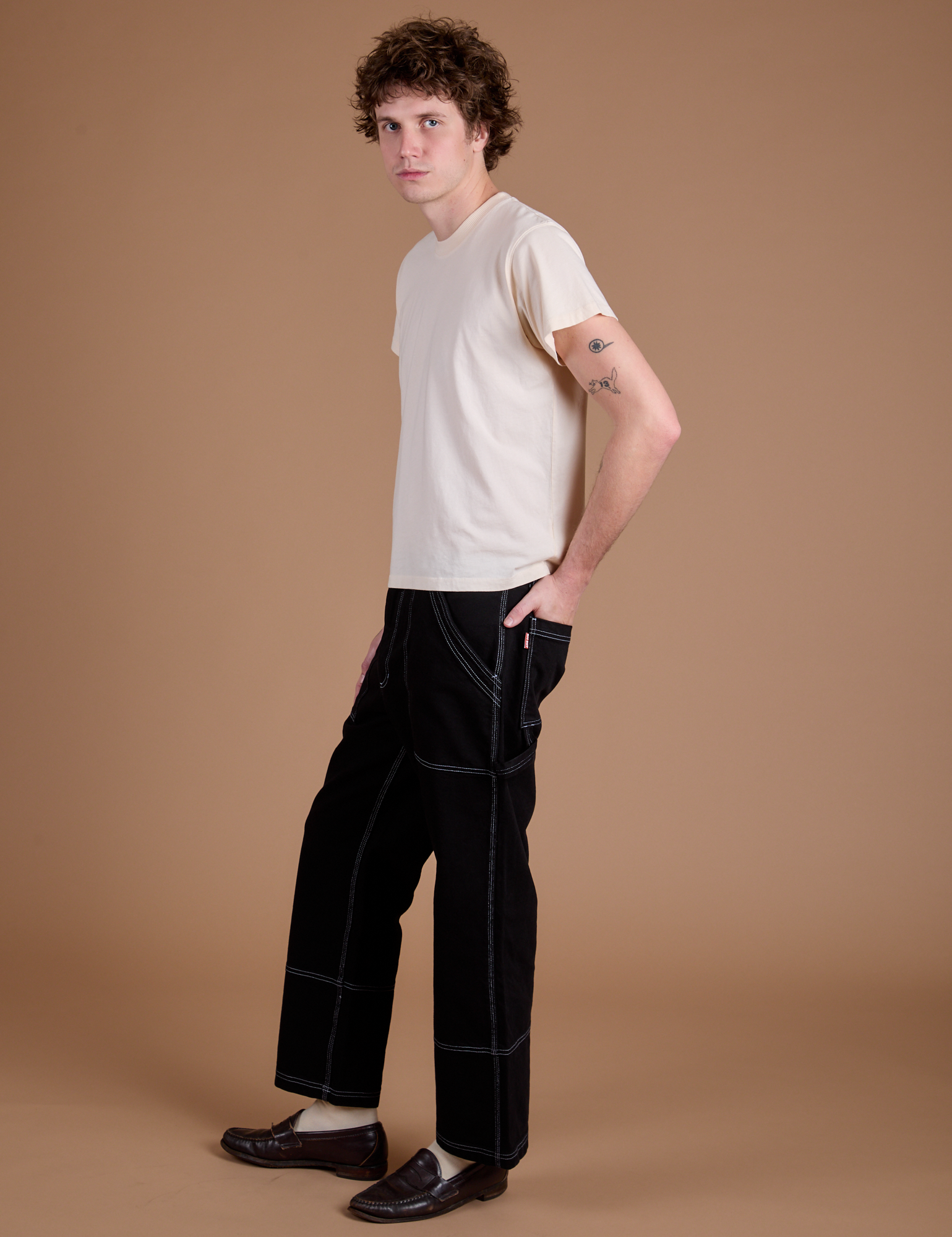 Side view of Carpenter Jeans in Black and Organic Vintage Tee in Vintage Tee Off-White on Quinn