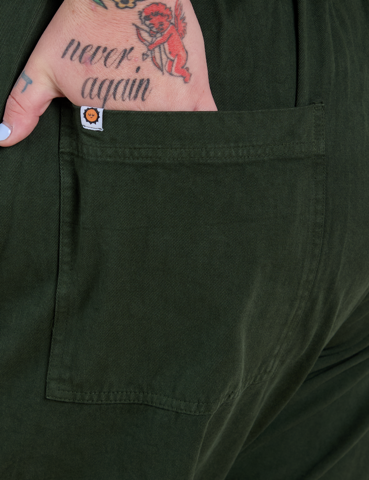 Close up of Sam's hand in the back pocket of Short Sleeve Jumpsuit in Swamp Green 
