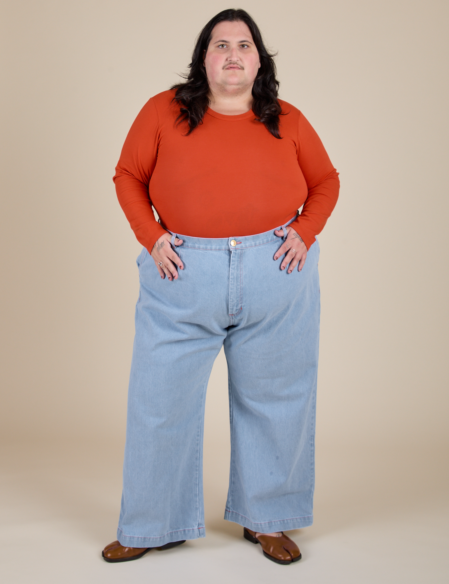 Sam is wearing Long Sleeve Baby Tee in Chili Red and light wash Indigo Wide Leg Trousers