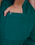 Close up of Alex's hand in the back pocket of the Hunter Green Action Pant