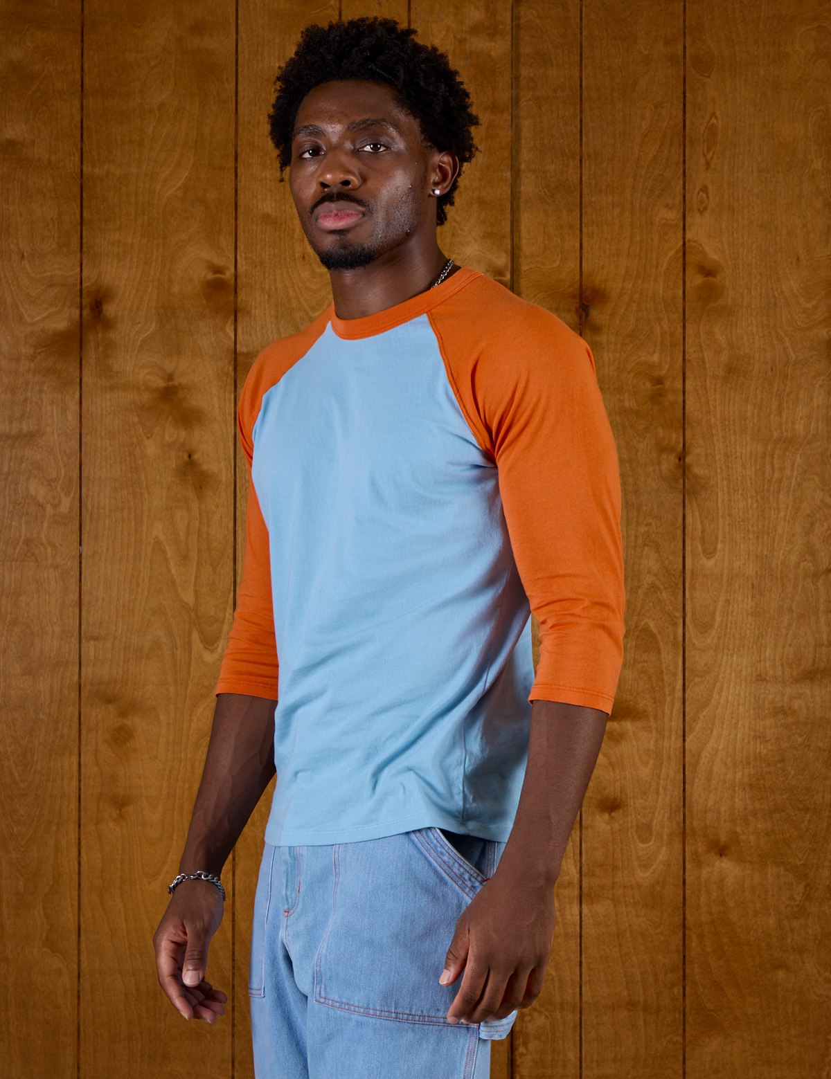 Angled side view of the Baby Blue/Orange Colorblock Raglan Tee on Isaac
