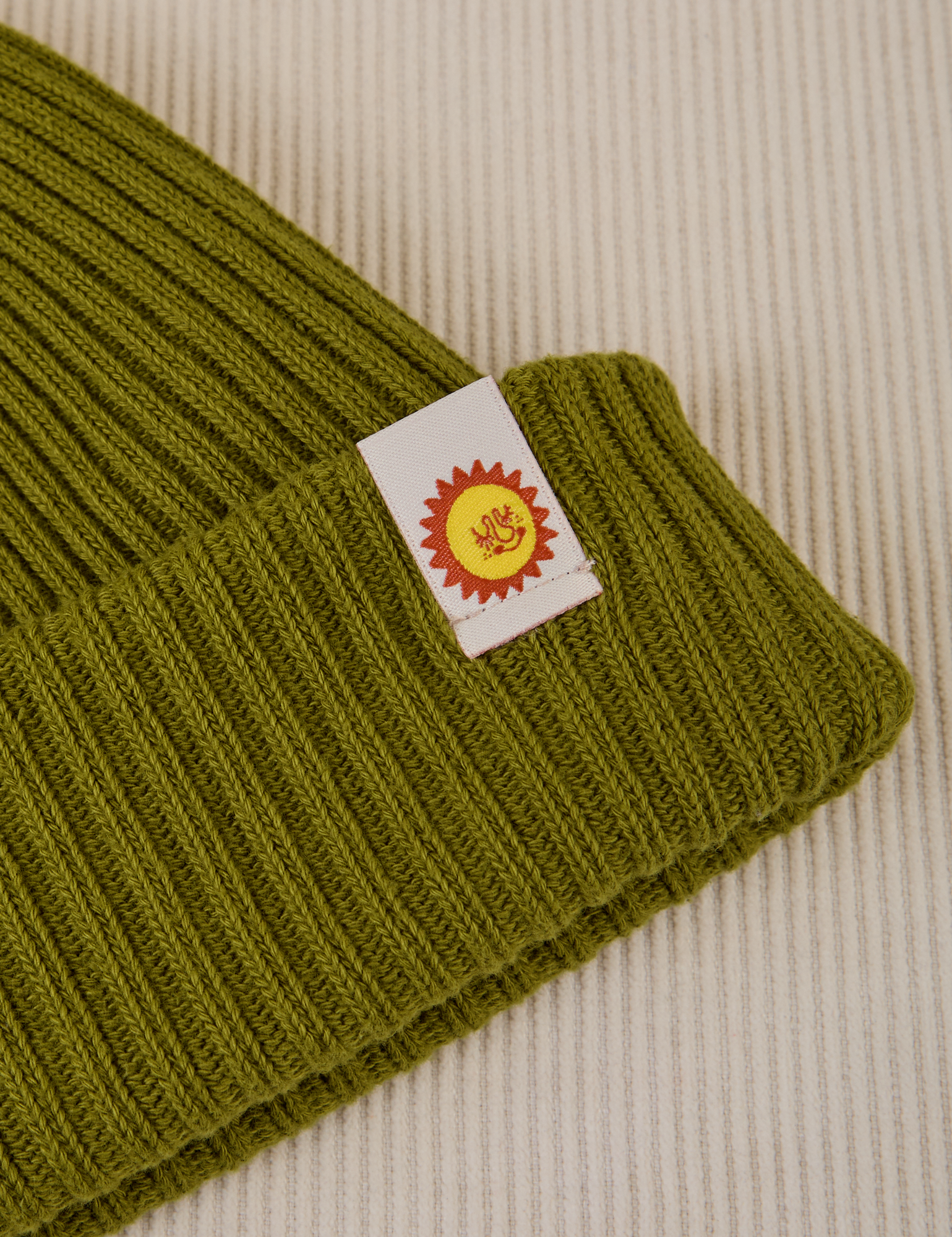 Ribbed Beanie in Olive Green close up of sun baby tag